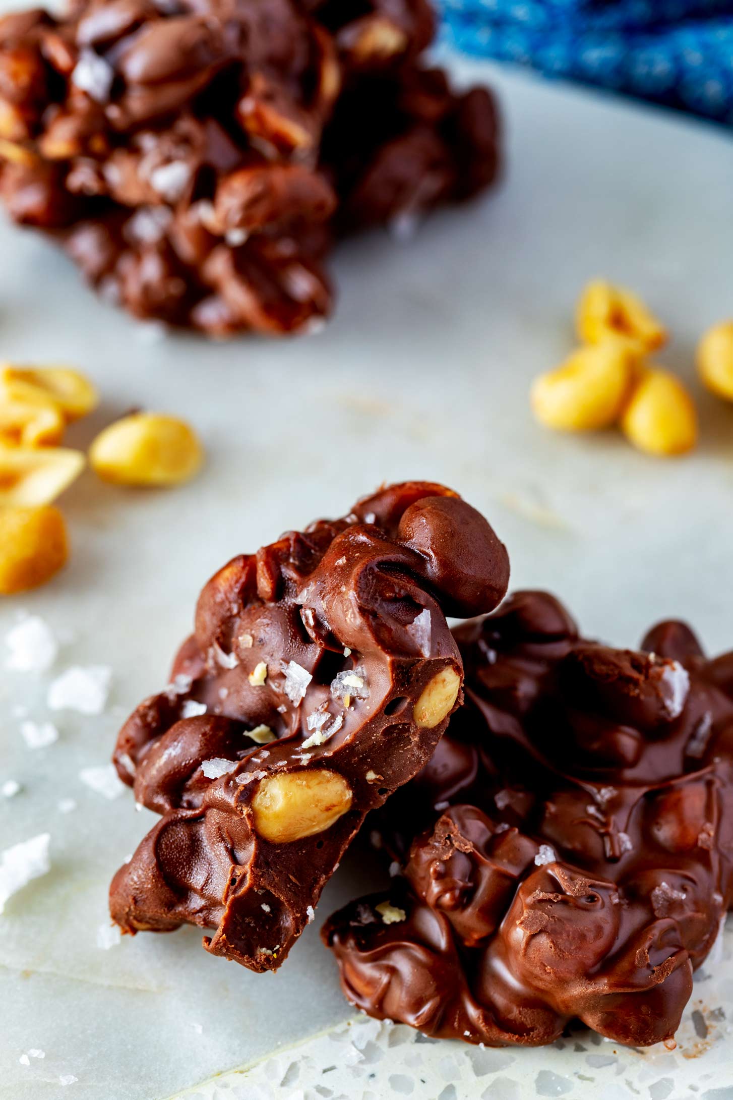 Close up photo of a chocolate peanut cluster with a bite out of it propped on another crockpot peanut cluster.