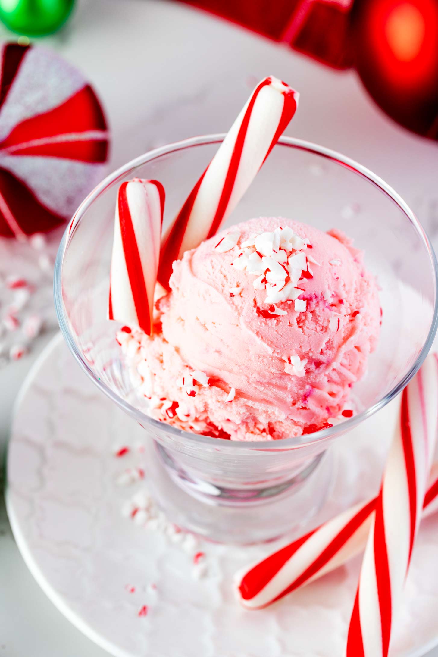 Photo of peppermint ice cream in a small glass ice cream dish sitting on a small white plate garnished with peppermint.