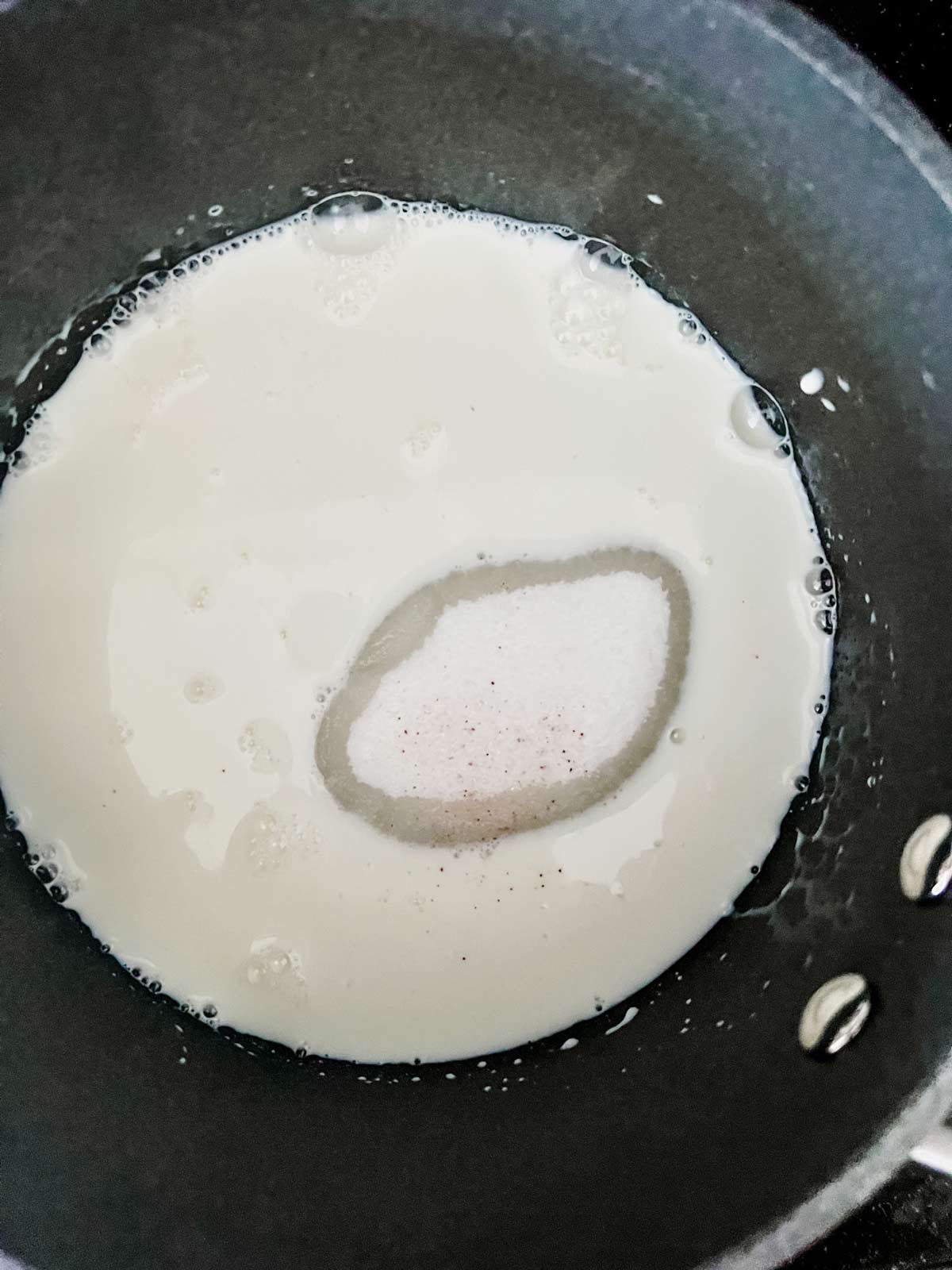 Milk, sugar and salt being cooked over medium heat in a saucepan.