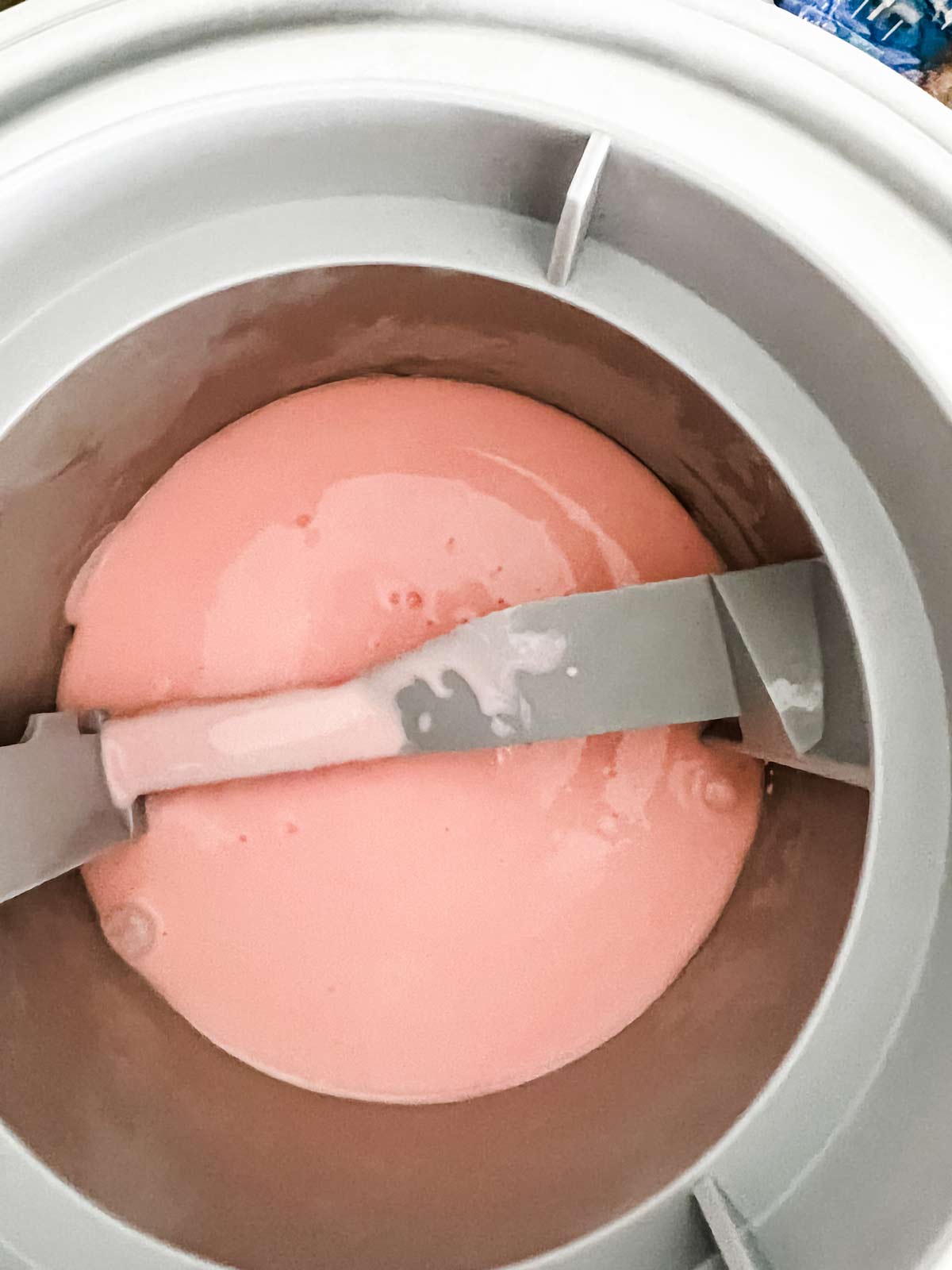 Pink peppermint ice cream in the bowl of an ice cream maker.