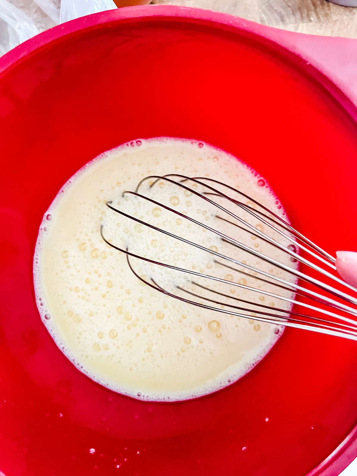 Eggs and a warm milk mixture being whisked together in a red bowl.