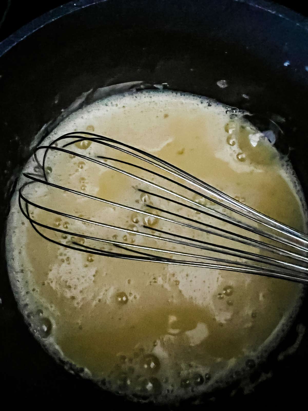 A mixture of milk, sugar, and eggs that have been mixed off the heat and are now cooking in a saucepan.