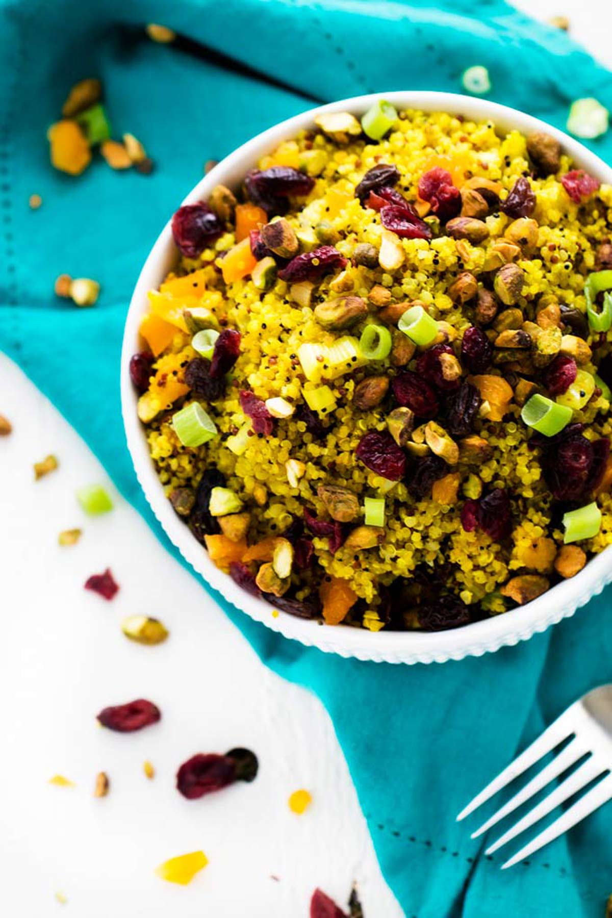 Close up overhead photo of a white bowl with a vegan quinoa salad sitting on a turquoise napkin.