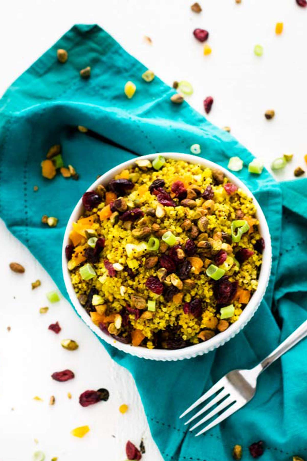Overhead photo of a white bowl with a vegan quinoa salad sitting on a turquoise napkin.