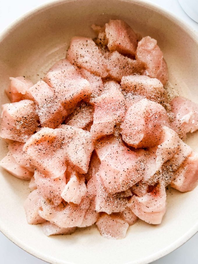 Chicken cubes seasoned with salt and pepper in a bowl.