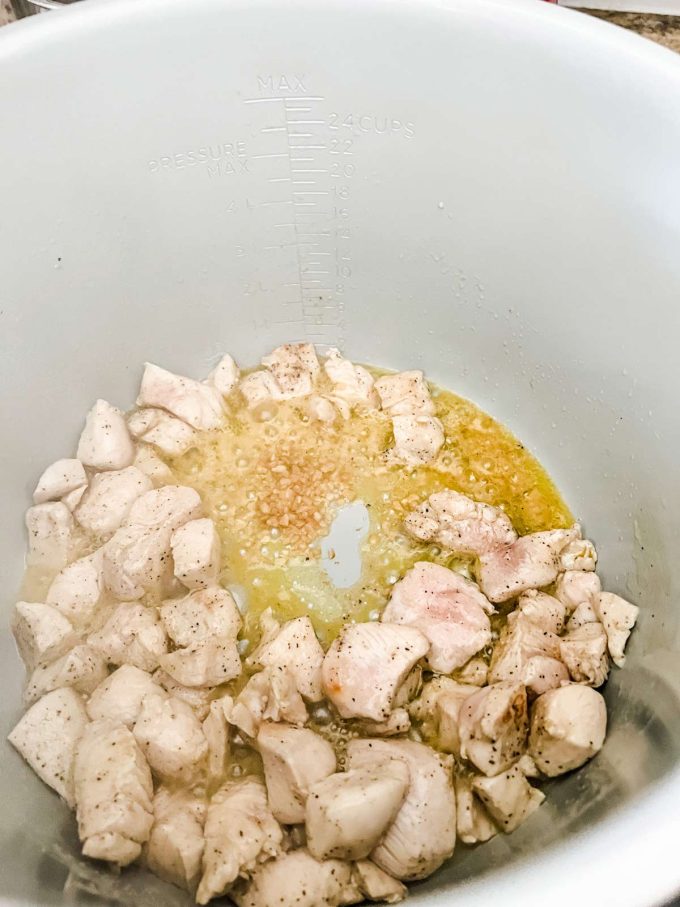 Seasoned chicken cubes and garlic cooking in butter in a a Ninja Foodi.