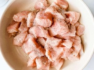 Chicken cubes seasoned with salt and pepper in a bowl.