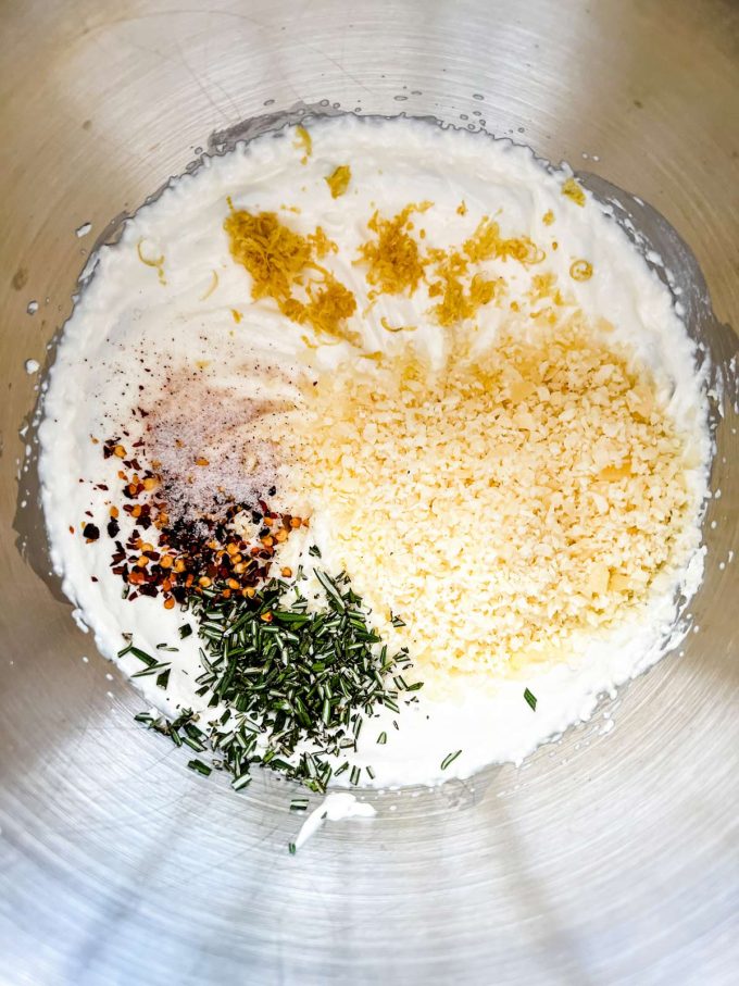 Photo of whipped ricotta cheese, heavy cream, parmesan, seasonings, lemon zest, and thyme in the bowl of a stand mixer.