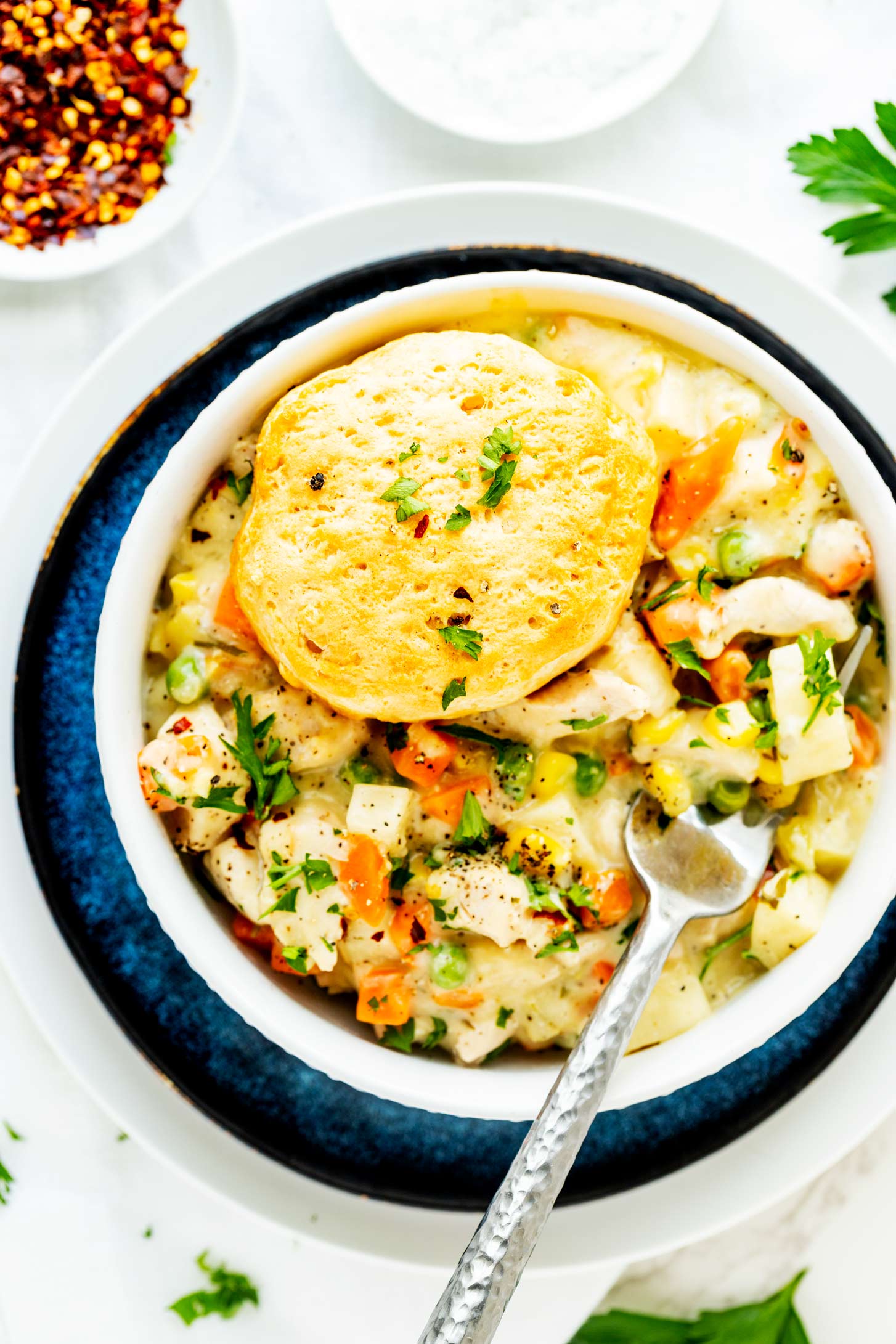 Overhead photo of a Crockpot chicken pot pie with biscuits served in a white bowl set on top of a blue plate.