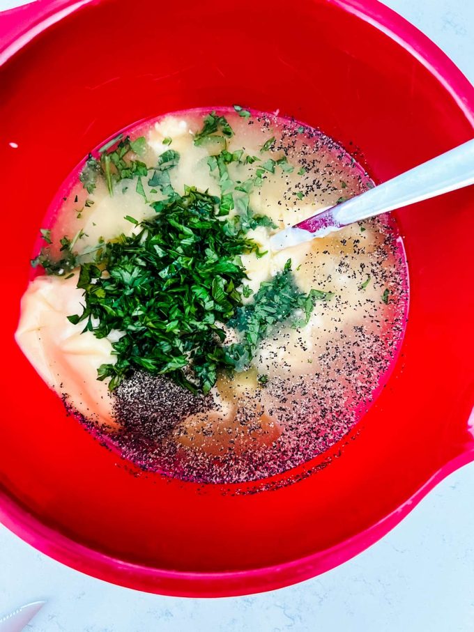 Photo of broth, cream of chicken, cream of celery soup, parsley and seasonings being mixed in a red bowl.