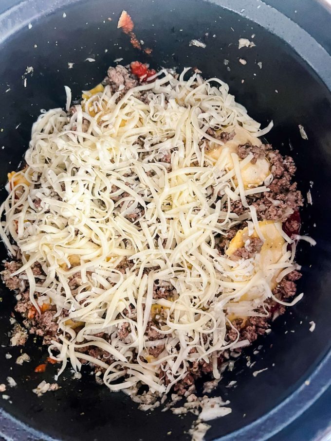 Marinara, ravioli, ground beef, and shredded mozzarella cheese in the inner pot of a slow cooker.