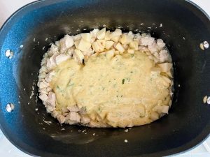 Chicken pot pie sauce being poured over chicken, onion, and potatoes in a slow cooker.
