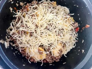Marinara, ravioli, ground beef, and shredded mozzarella cheese in the inner pot of a slow cooker.