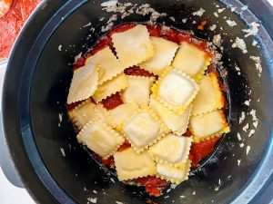 Marinara in the bottom of a slow cooker topped with frozen ravioli.