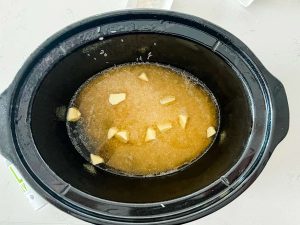 A crockpot with white rice and broth topped with butter.
