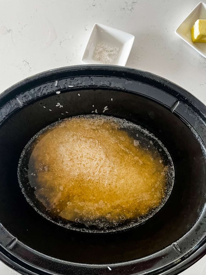 Broth covering white rice in a slow cooker.
