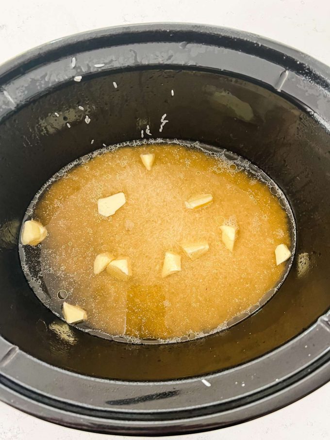 A slow cooker with white rice, salt, broth, and butter.