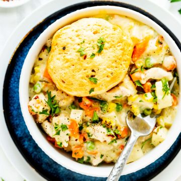 Square overhead photo of a crockpot chicken pot pie with biscuits in a white bowl sitting on a blue plate.
