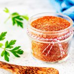 Close up square photo of a homemade BBQ seasoning in a small glass jar.