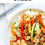 A plate of Blackstone Stir Fry with chicken, red bell peppers, zucchini, onions, and sesame seeds served over white rice sits next to a fork on a white surface. The text reads Stir Fry on the Blackstone Griddle.