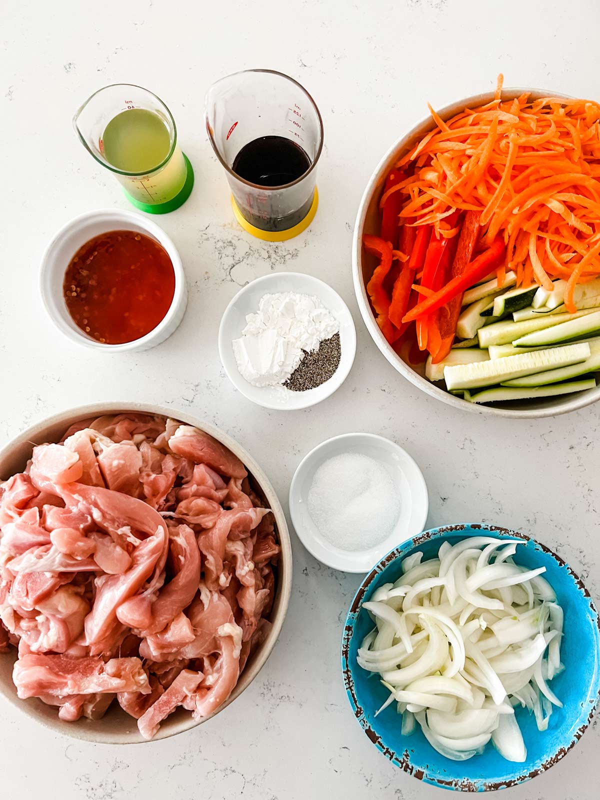 Overhead photo of chopped chicken thighs, carrots, red pepper, zucchini, onion, chicken broth, soy sauce, chili sauce, sugar, cornstarch, and black pepper.