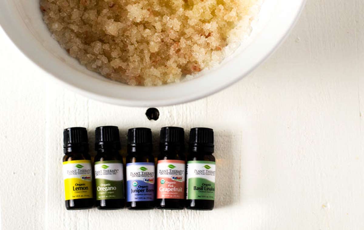 Photo of a bowl of salts sitting next to five small bottles of essential oils.