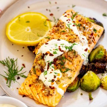 Square photo of garlic salmon with lemon dill sauce on a plate with Brussel sprouts.