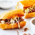 Square close up photo of a halved slow cooker french dip with a small dish of jus next to it.