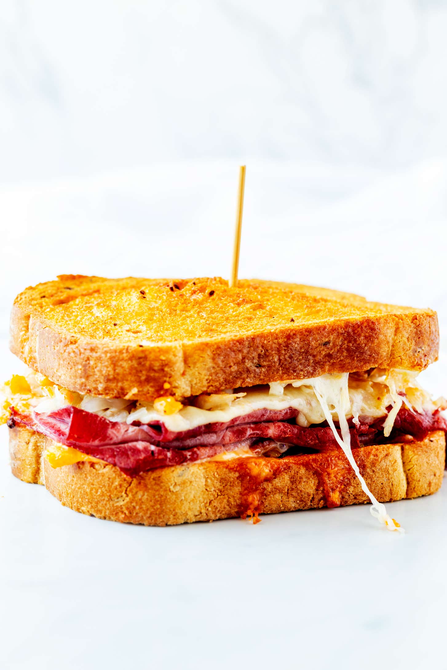 Photo of an air fryer Reuben with a skewer through it on a white background.