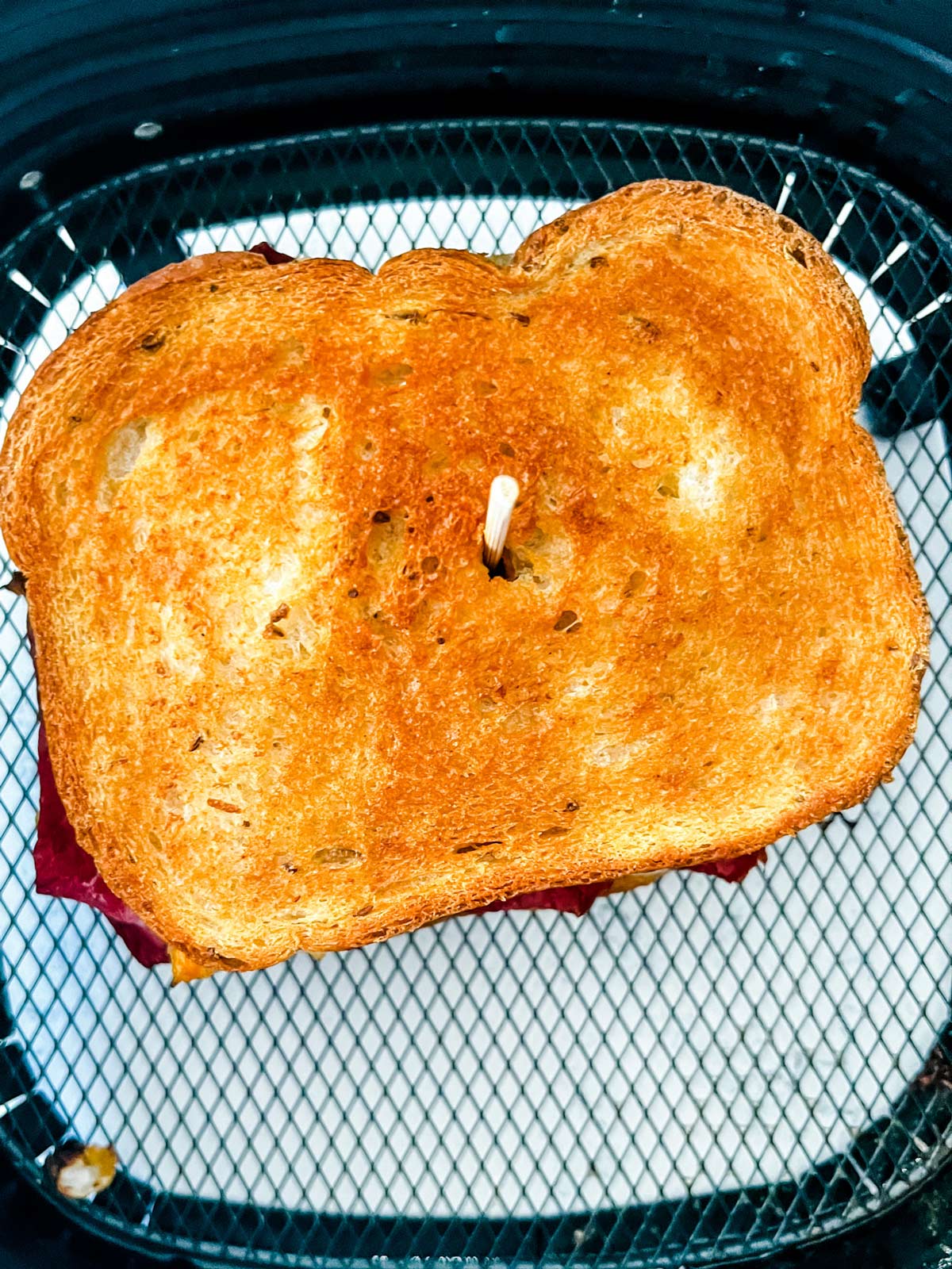 A crispy air fryer Reuben sandwich that is in an air fryer basket after just being cooked.