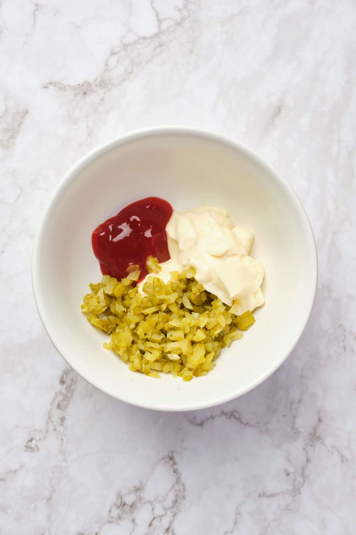 Photo of mayonaise, ketchup, and dill pickles in a small bowl.