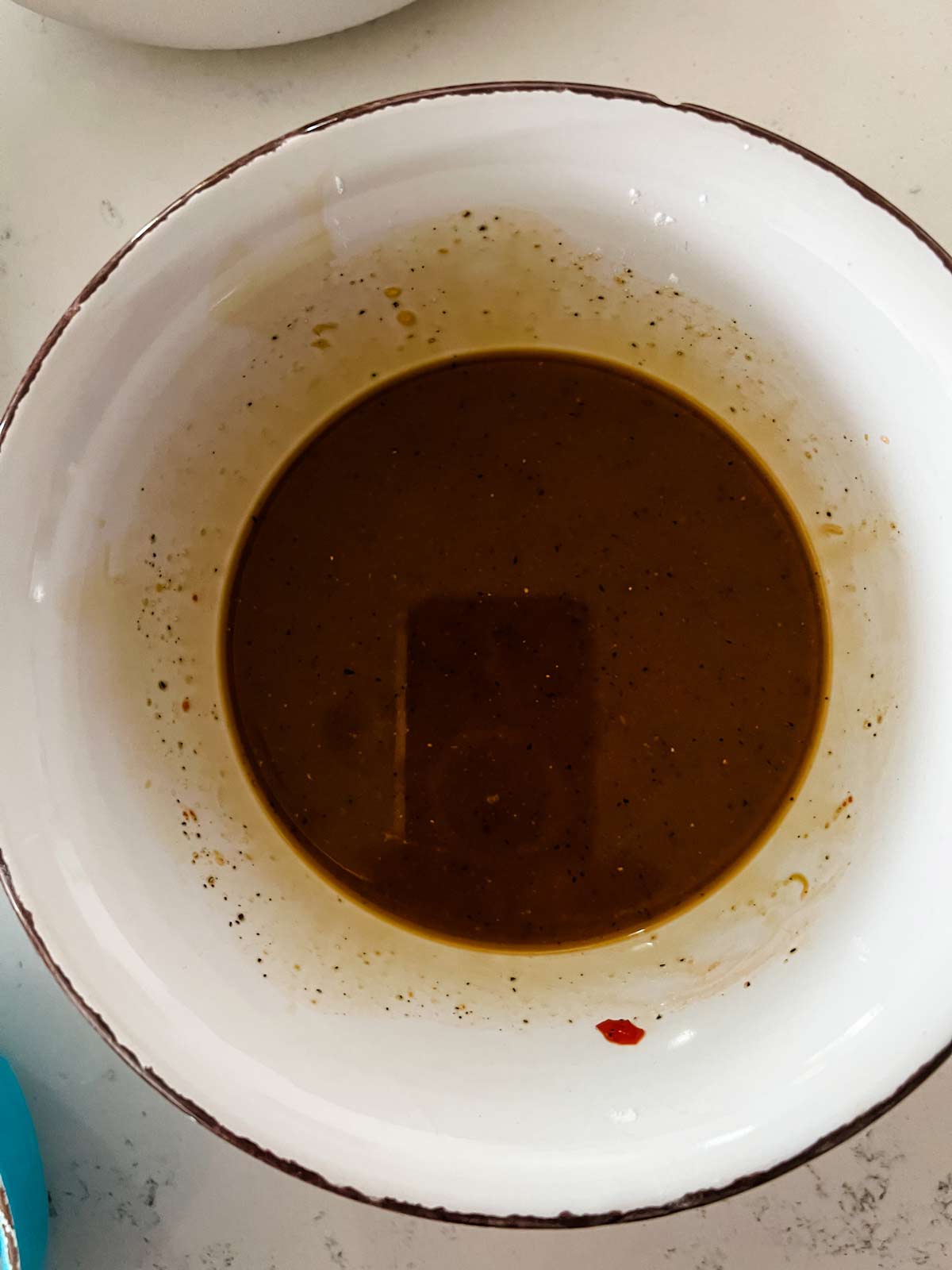 Photo of chicken broth, soy sauce, chili sauce, sugar, cornstarch, and black pepper that have been whisked together in a bowl.