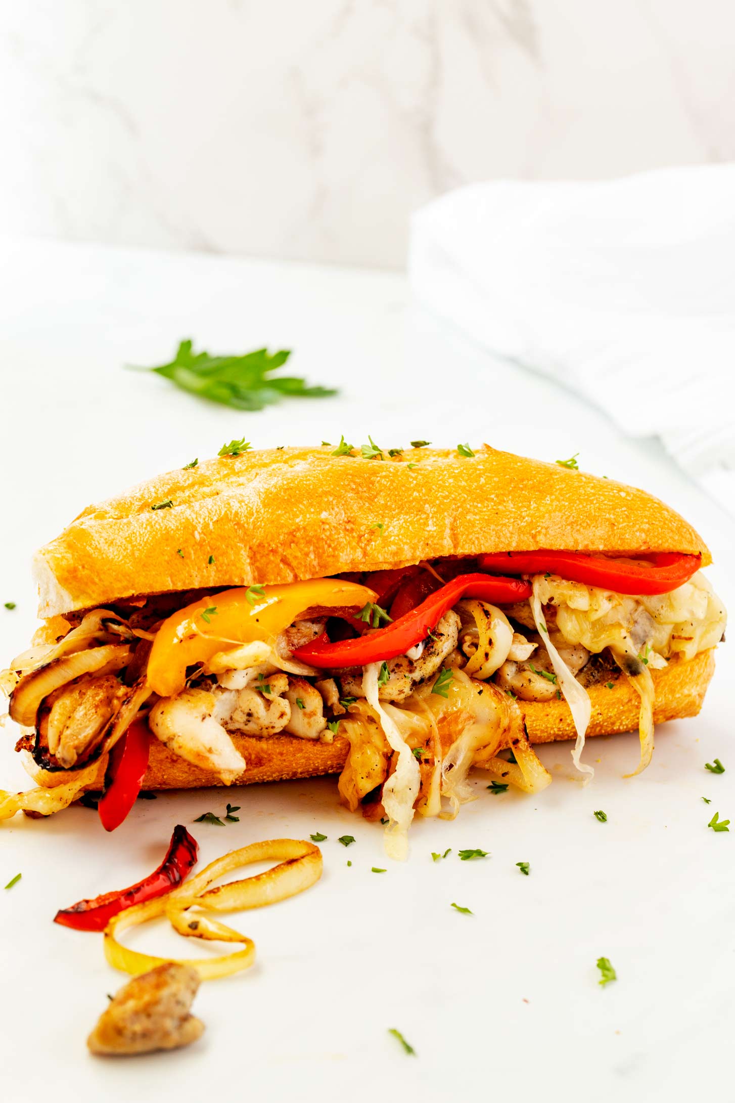 A white countertop with a chicken philly cheesesteak garnished with parsley.