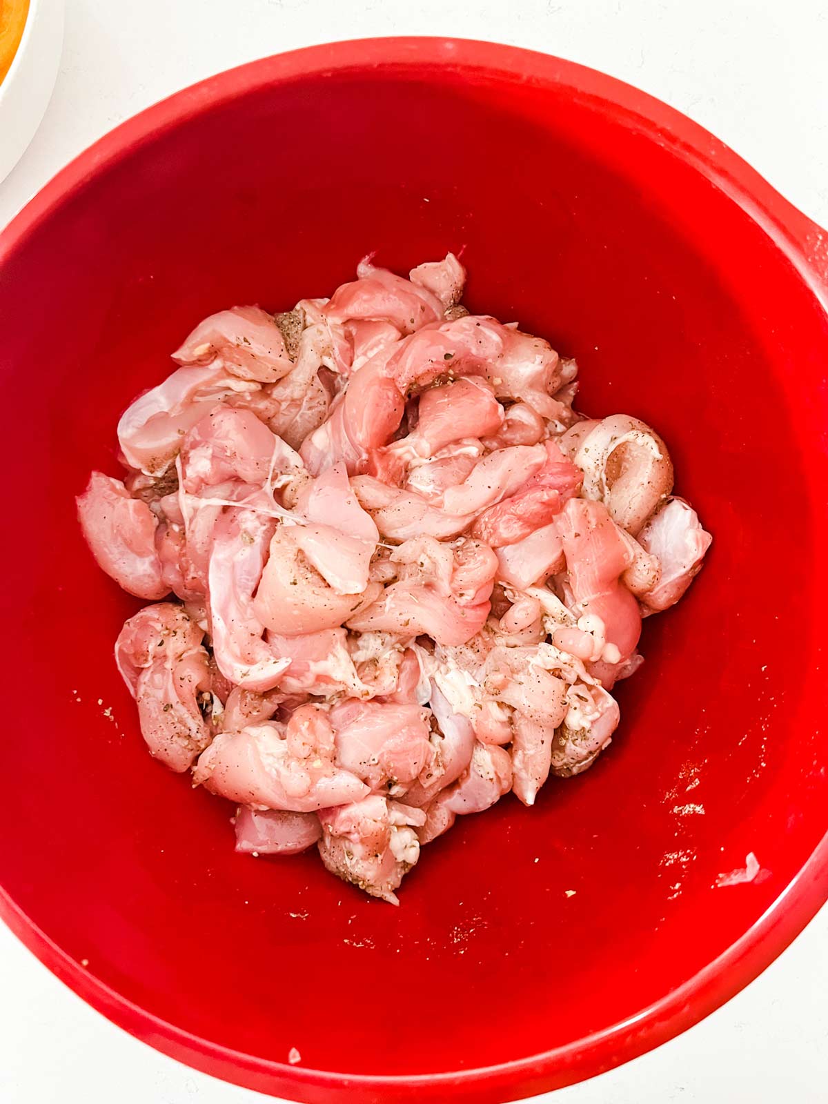 Seasoned sliced chicken thighs in a red bowl.