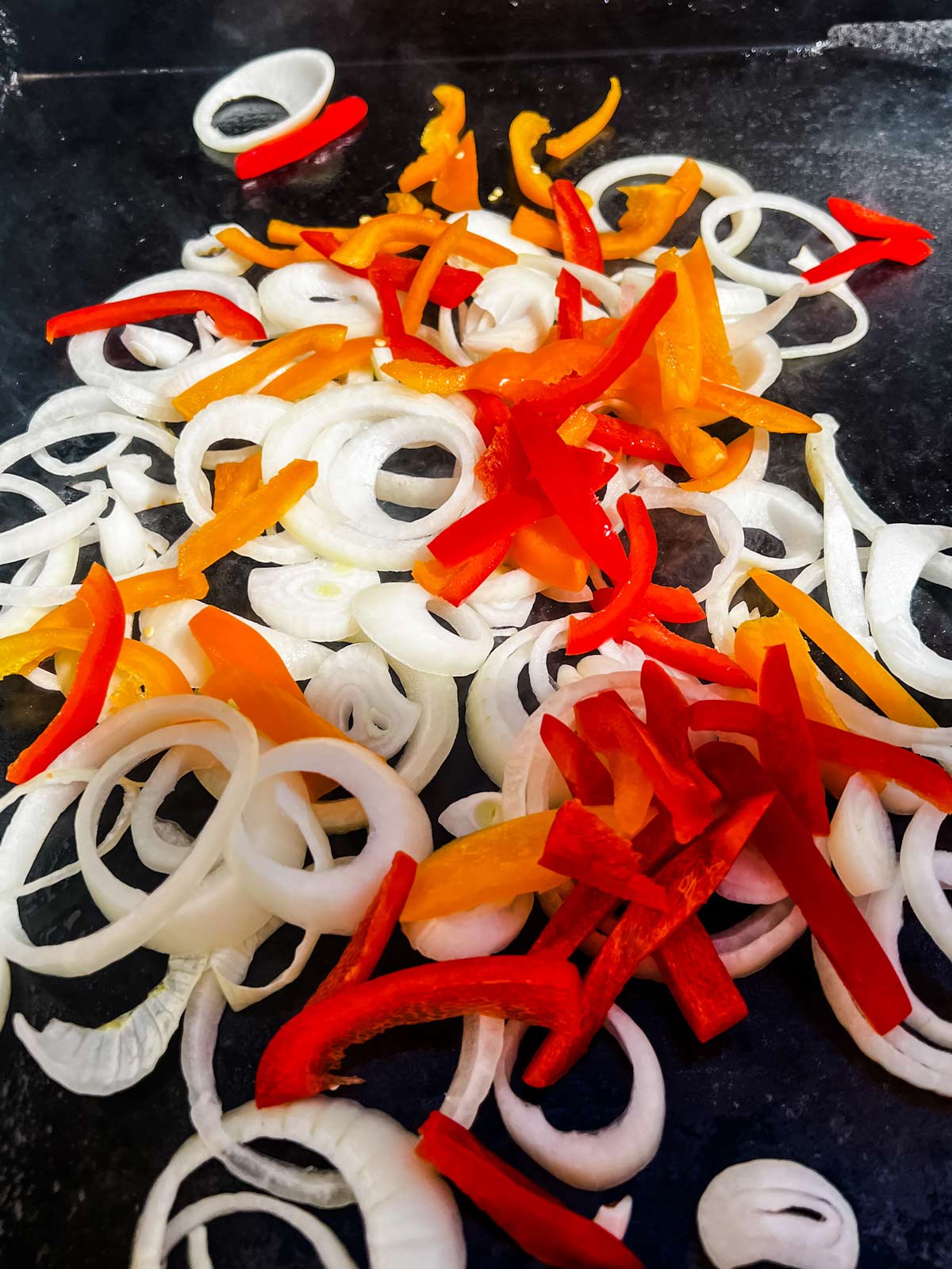 Sliced onions and peppers that have just been added to a Blackstone griddle.
