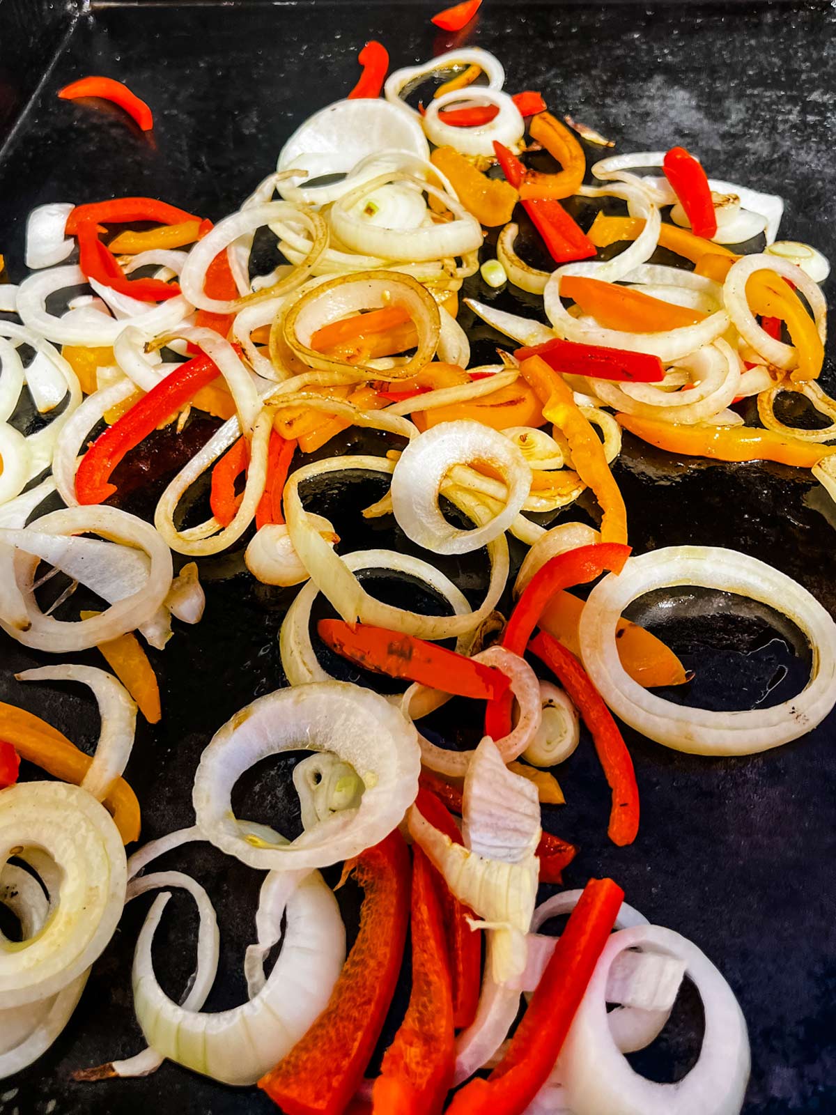 Peppers and onions cooking on a flat top griddle.
