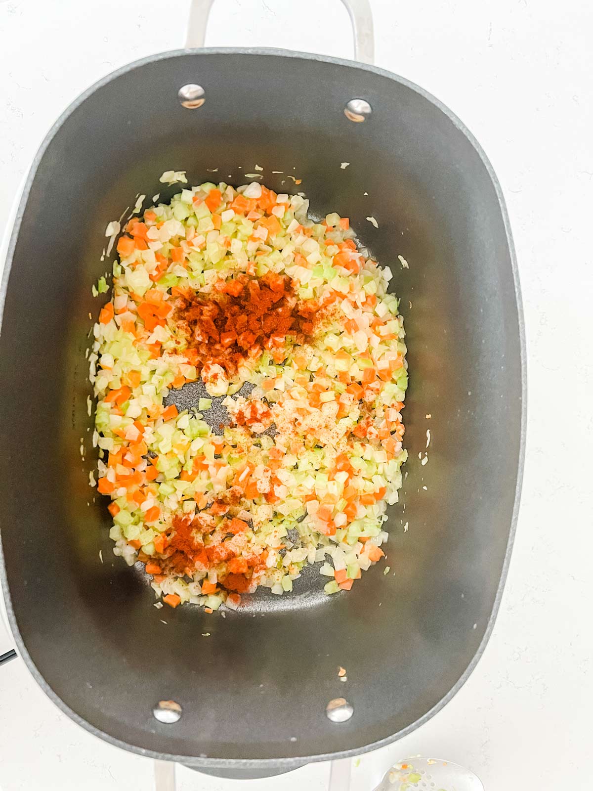 Photo of seasonings sprinkled on top of sauteed onion, celery, and carrots.