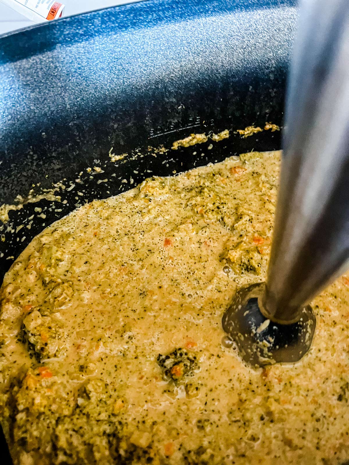 An immersion blender blending broccoli cheese soup in a slow cooker.