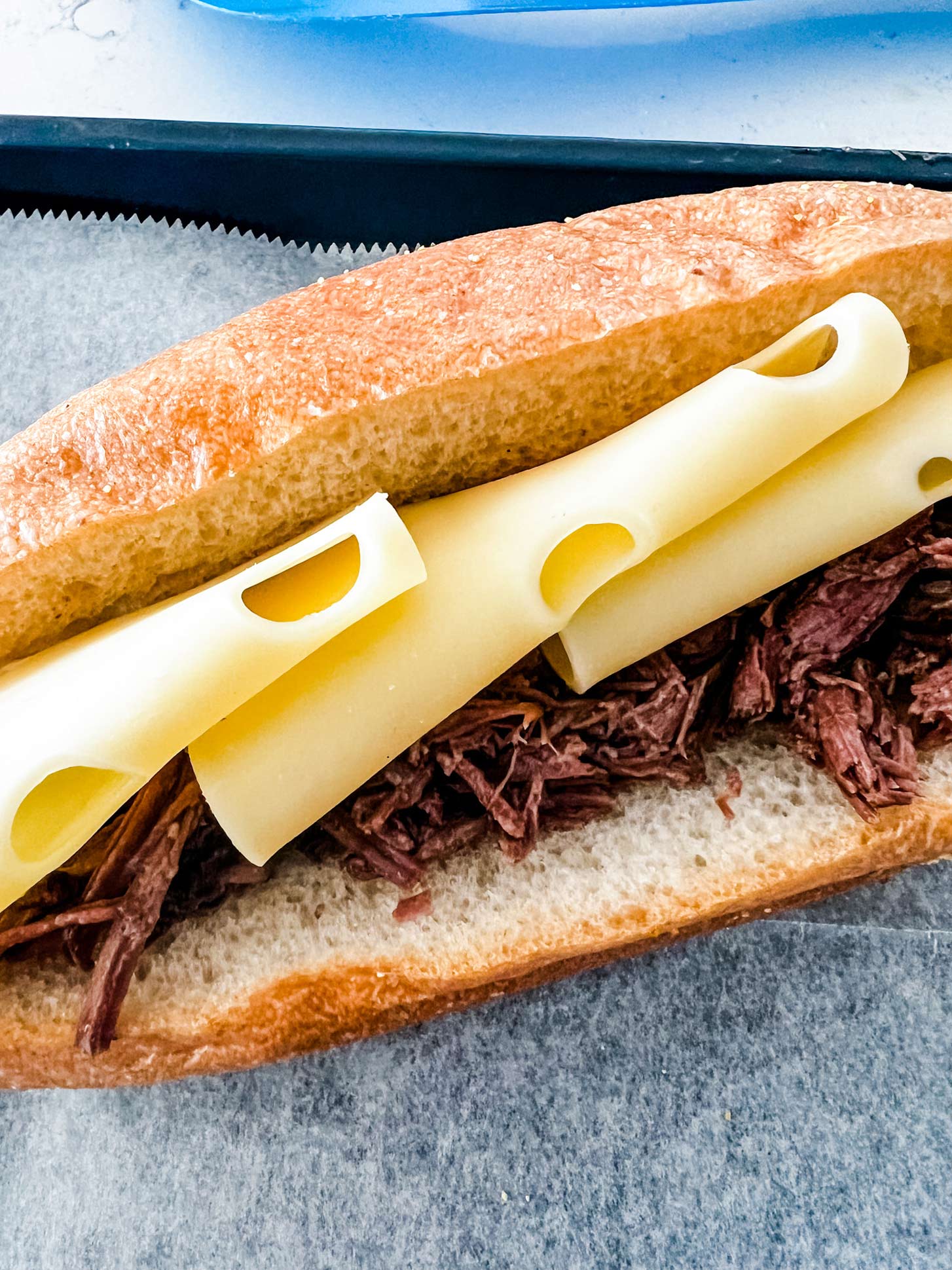 A French dip sandwich with cheese slices on a parchment lined baking sheet.