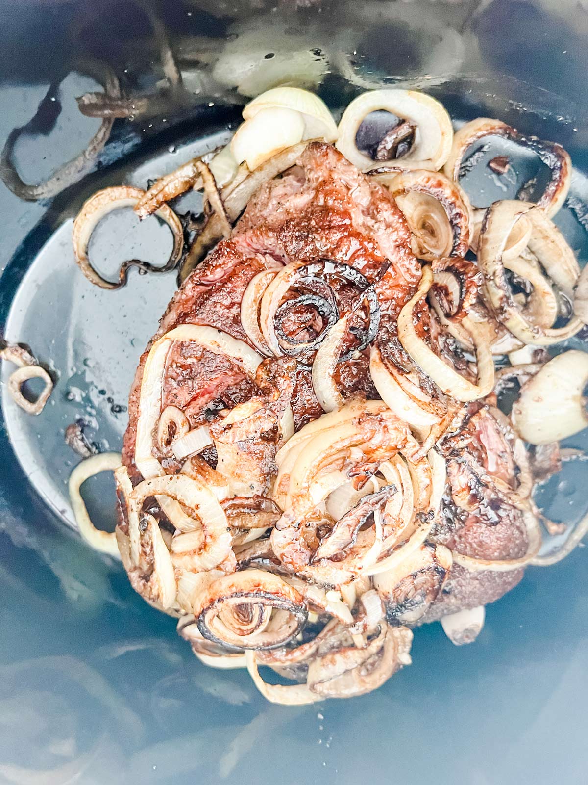 Overhead photo of a slow cooker with a seared roast and onions in it.