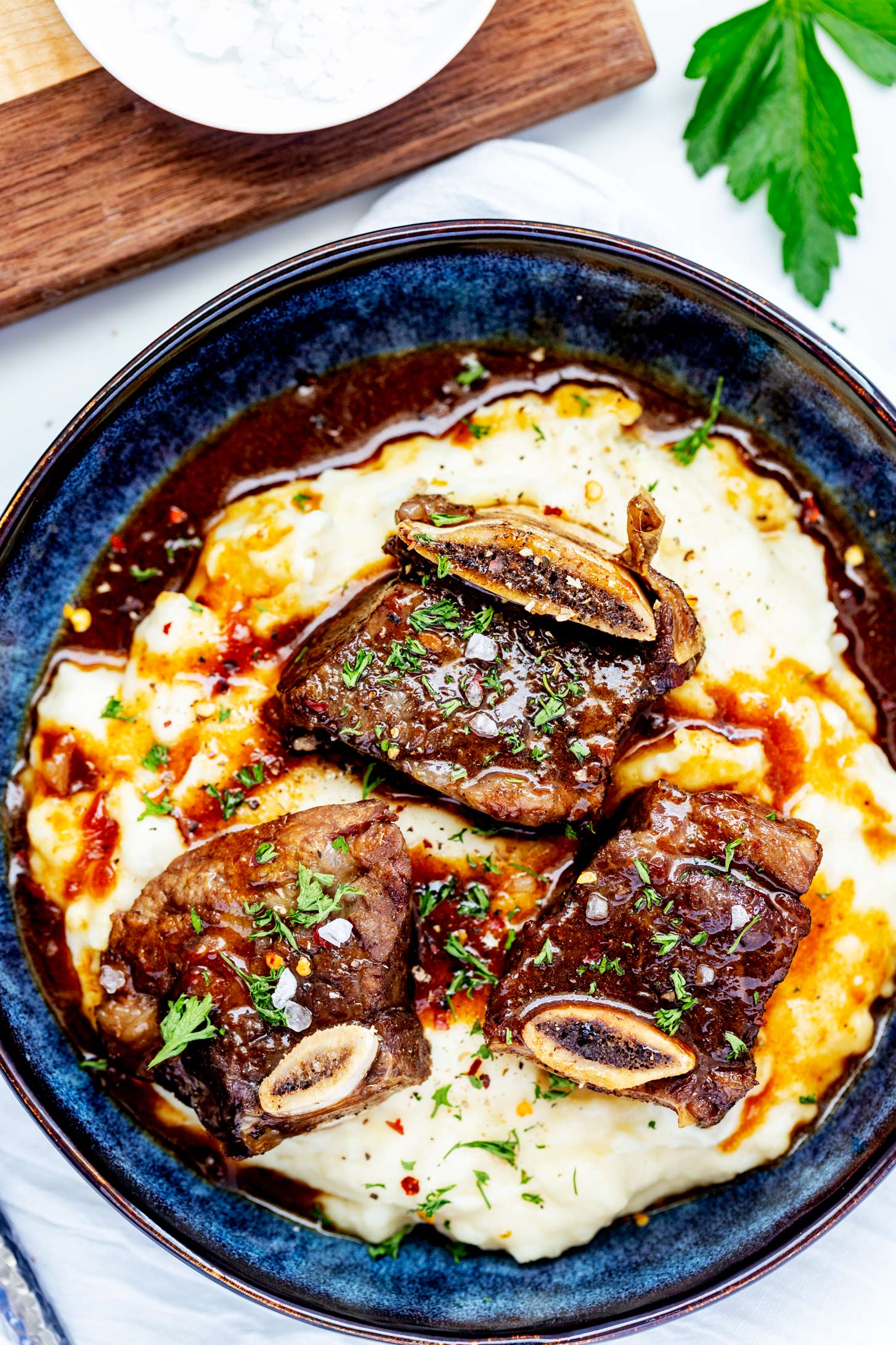 Instant Pot Short Ribs on top of mashed potatoes with gravy in a shallow blue bowl.