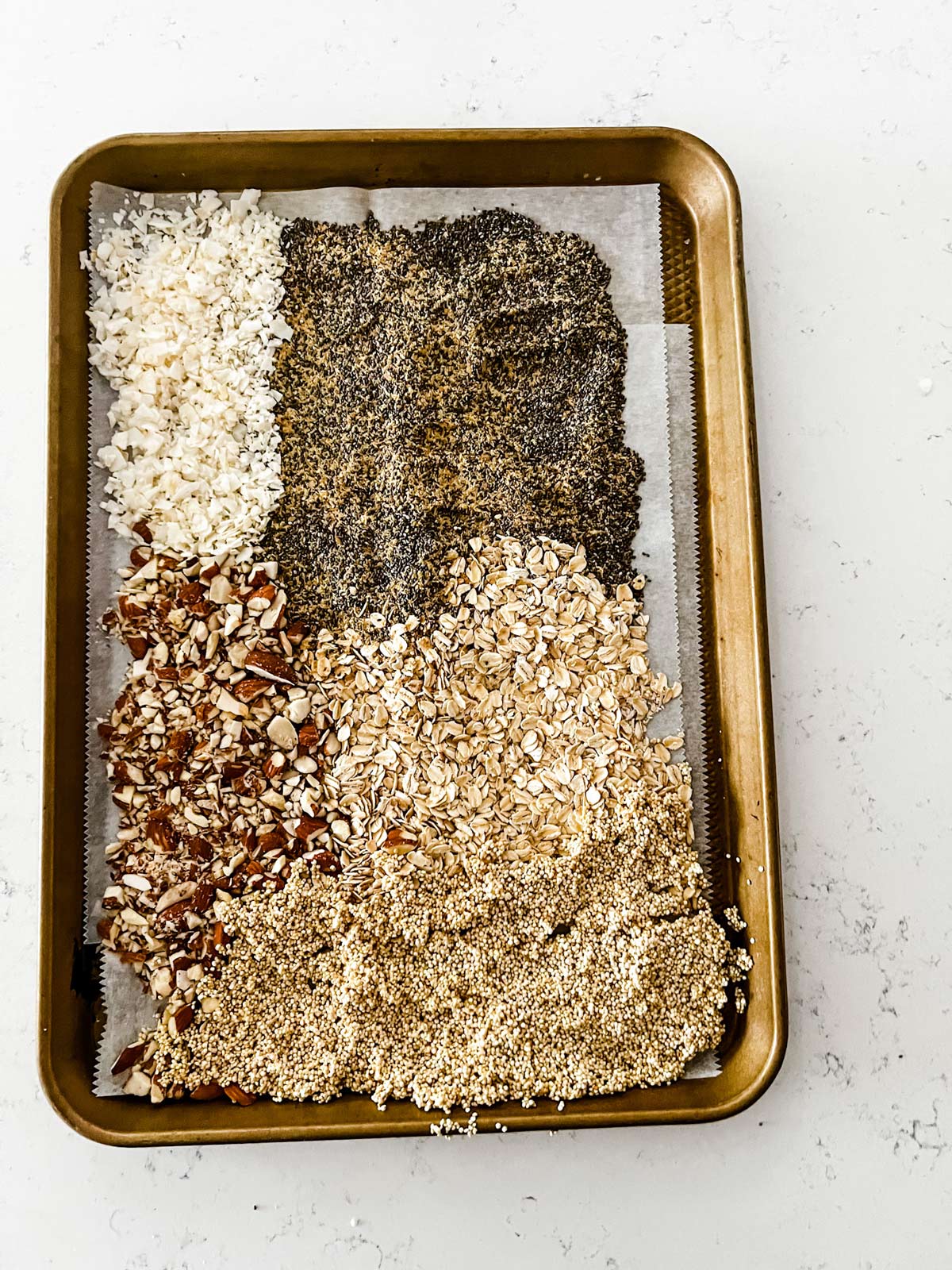 Photo of Quinoa, chia seeds, flax seeds, shredded coconut, oatmeal, and almonds on a parchment lined sheet pan.