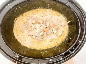 Chicken on top of a creamy sauce and pasta in a slow cooker.
