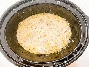 Pasta cooking with a creamy sauce and chicken in a slow cooker.