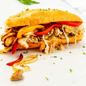 Photo of a chicken philly garnished with parsley on a white countertop.