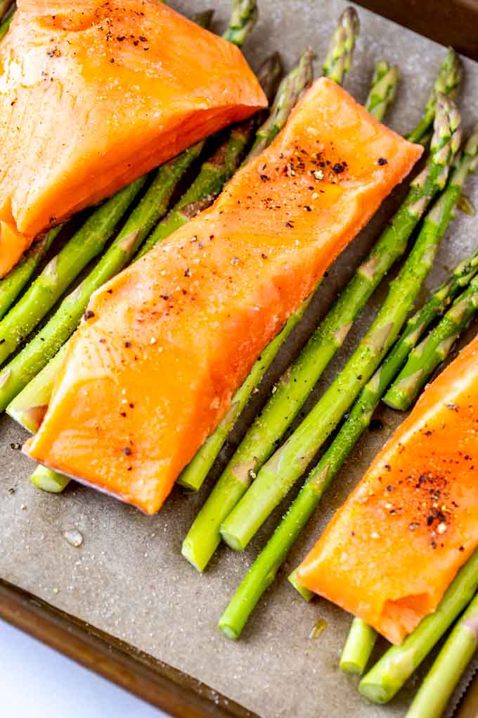 Photo of seasoned salmon and asparagus on a parchment lined sheet pan.