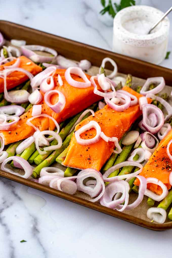 Photo of asparagus, salmon, and shallots on a sheet pan.