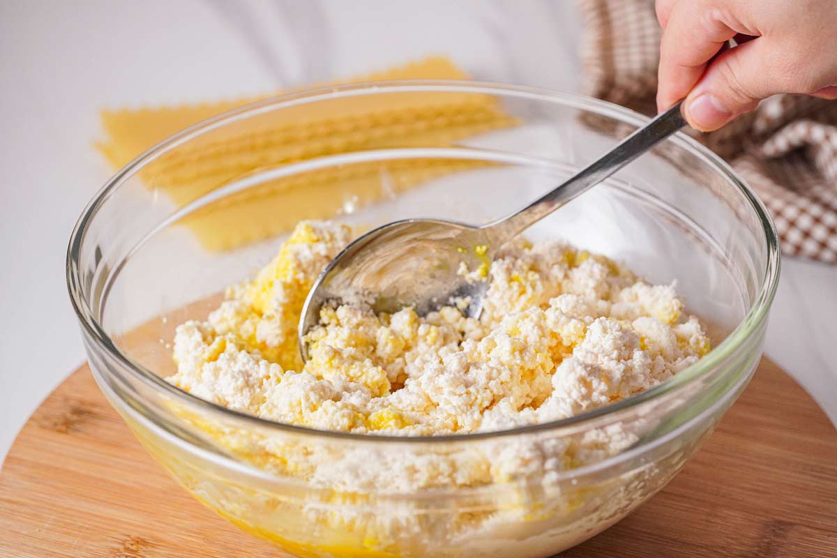 Ricotta cheese, egg, and parmesan in a bowl being mixed together.