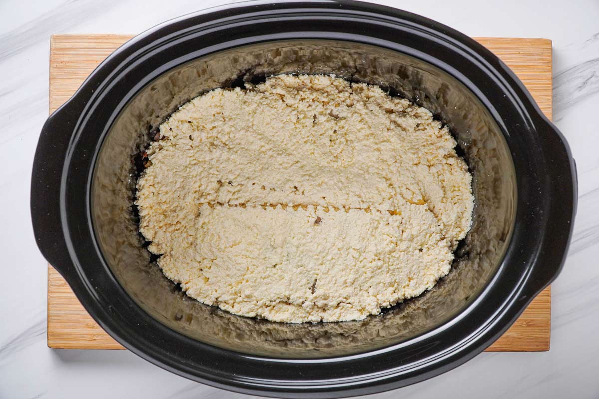 A ricotta mixture over lasagna noodles in a slow cooker.
