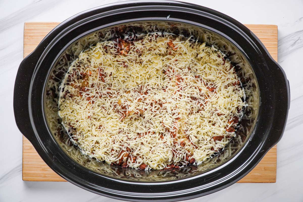 Cheese added to a crockpot lasagna in a slow cooker.